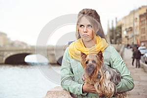 Sad young woman with small dog on the embarkment, waiting friend.