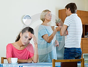 Sad young woman watching husband and mother having fight