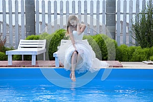 Sad young woman in white dress sitting near the pool