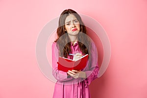 Sad young woman writing her feelings in diary, looking upset and gloomy, feeling heartbroken, sharing memories in