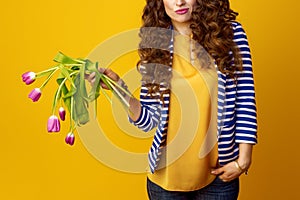 Sad young woman on yellow background holding wilted flowers