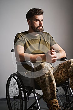 Saddened military man sitting in a wheelchair at the hospital and thinking