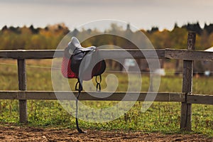 A saddle hangs on a wooden fence