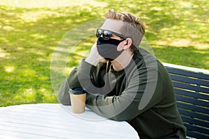 Sadness Man in a protective black mask sitting at a table in a cafe. Virus protection. Men in a mask drinking coffee in