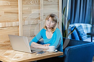 Sadness tired young girl freelancer with blonde bob haircut hair in blue t-shirt are sitting alone in cafe and searching for a