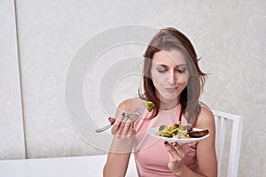 Sad women is on dieting time looking at broccoli on the fork. girl do not want to eat vegetables and dislike taste of