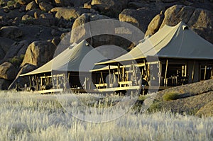 Safari camp in Africa, tents in front of huge boulders. Luxury safari tents with patio in evening light