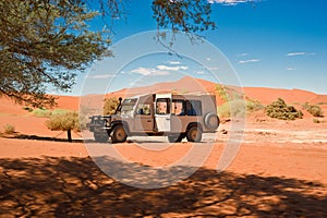 Safari jeep between orange dunes in Namibia. Landscape in Namib Desert, Namibia