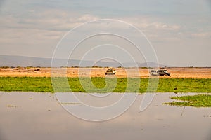 A safari van on a dirt road in the panoramic savannah grassland landscapes of Amboseli National Park in Kenya