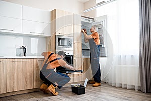 Safe and affordable repairs. Two handymen, workers in uniform fixing, installing furniture and equipment in the kitchen