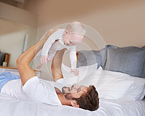 Safe in daddys hands. a father lying on a bed holding his baby girl up in the air.