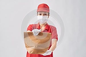 Safe delivery for quarantine woman in red dress, face mask and gloves gives paper bag