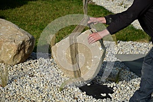 Safe handling of a very heavy granite boulder with a crane, the stone is picked up and tied with straps and placed in a hole a glo