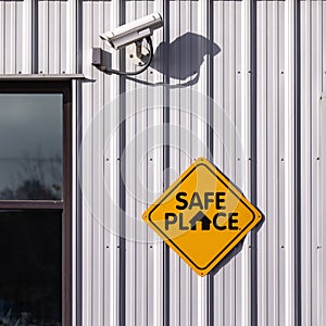 `Safe place` sign of a light metal wall of a building with a CCTV security cam above it