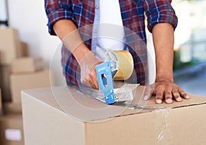 Safe and sealed. Shot of an unidentifiable man using a tape dispenser to close a box while moving house.