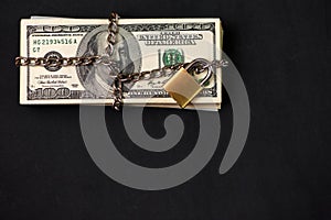 Safe secure chain locked stack of hundred dollar bills on dark background with copy space