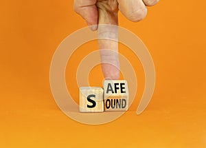Safe and sound symbol. Businessman turns a wooden cube and changes the word `safe` to `sound` or vice versa. Beautiful orange
