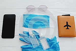 Safe travel in summer 2020. Blue face mask, gloves, antiseptic and disinfectant, passport, sunglasses and phone on white