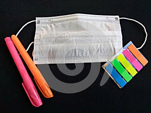 Safely return to school. School supplies and medical mask for protection against coronavirus or covid-19 on black background.