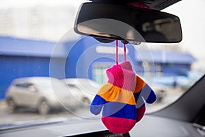 Safety of baby in car. children`s mittens with blue, orange and pink stripes hang on the rear view mirror of a modern