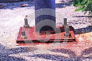 Safety concept. Rusty nut is attached to steel plate of base of electric pole standing outdoors in park.