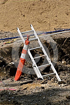 Safety cone recognizes danger where a ladder reaches out of a trench