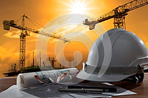 safety helmet and architect pland on wood table with sunset scene and building construction