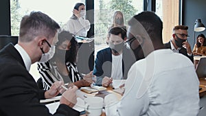 Safety measures at busy office. Young multiethnic happy business people working together at meeting wearing face masks.