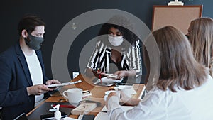 Safety measures at workplace after quarantine ending. Happy diverse business people wear masks working at office table.