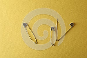 Safety pins on yellow background, flat lay