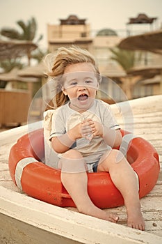 Safety, rescue and help concept. Happy child sit in ring buoy on sunny day. Little boy with lifebuoy on tropical beach