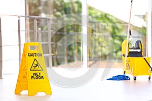 Safety sign with phrase Caution wet floor mop bucket, indoors. Cleaning service