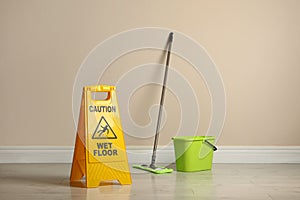 Safety sign with phrase Caution wet floor, mop and bucket indoors. Cleaning service