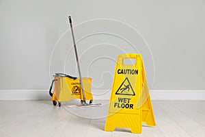 Safety sign with phrase Caution wet floor, mop and bucket indoors. Cleaning service