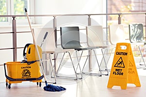 Safety sign with phrase Caution wet floor and mop bucket, indoors