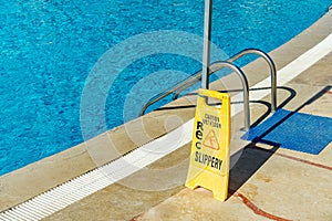 Safety sign with phrase Caution wet floor near the swimming pool at the tropical resort. Cleaning service slippery