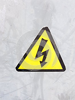 a safety sign yellow and black on silver metal background electric bolt in triangle safety caution careful