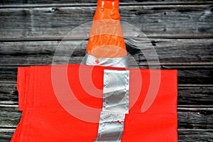 safety vest with reflective stripes and a car traffic security cone  on wooden background, selective focus of