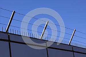 Safety wall with barbed wire and spikes on top of a fence provide security - blue sky background