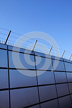 Safety wall with barbed wire and spikes on top of a fence provide security - blue sky background