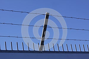 Safety wall with barbed wire and spikes on top of a fence provide security - blue sky background