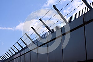 Safety wall with barbed wire and spikes on top of a fence provide security - blue sky background