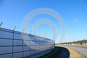 Safety wall with barbed wire and spikes on top of a fence provide security - blue sky background