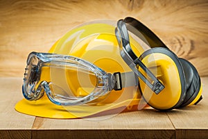 Safety of work. construction safety tools. yellow helmet blue goggles and earphones on wood background