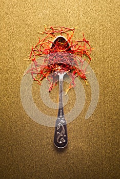 Saffron in a metal spoon. Spicy seasoning isolated on golden, top view