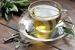 Sage herbal tea in a glass cup with fresh and dried leaves on rustic wooden background