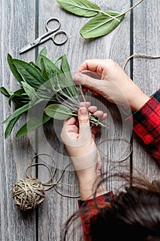 Sage leaf bundle in hands, prepare herbs to dry, hemp string wooden background overhead view