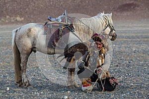 Kazakh Eagle Hunter Berkutchi with horse while hunting to the hare with a golden eagles on his arms