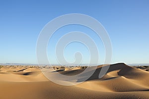 Sahara desert sand dunes with clear blue sky.