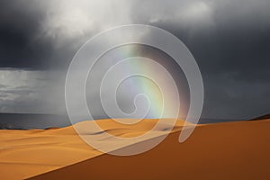 Sahara desert sand dunes with rainbow against dark, cloudy, rainy sky